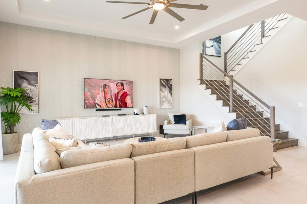 Living room with large couch, wall-mounted TV, and stairway to upper level in an elegant 8-bedroom Bear’s Den Resort Orlando residence.
