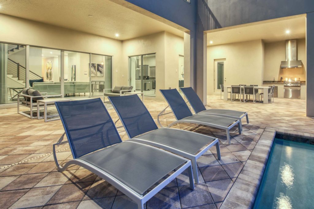 Lounge chairs next to a private pool, with summer kitchen and covered seating at an elegant 8-bedroom Bear’s Den Resort Orlando residence.