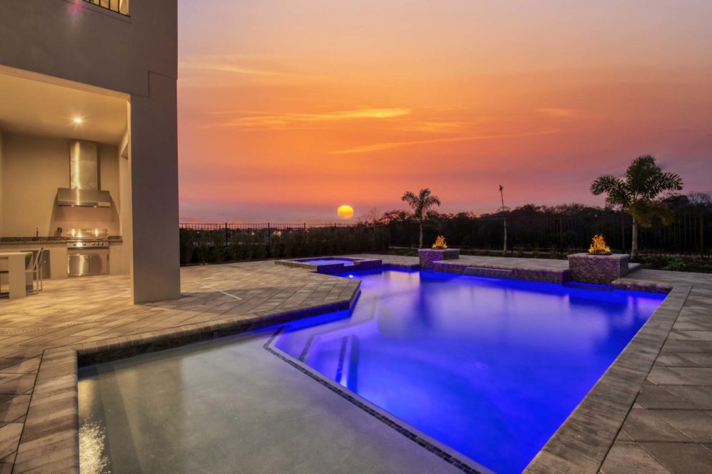 The sun sets behind a lit private pool and fire pits at an elegant 8-bedroom Bear’s Den Resort Orlando residence.