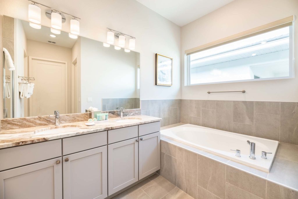 Bathroom with drop-in bathtub, double sink, and large mirror.