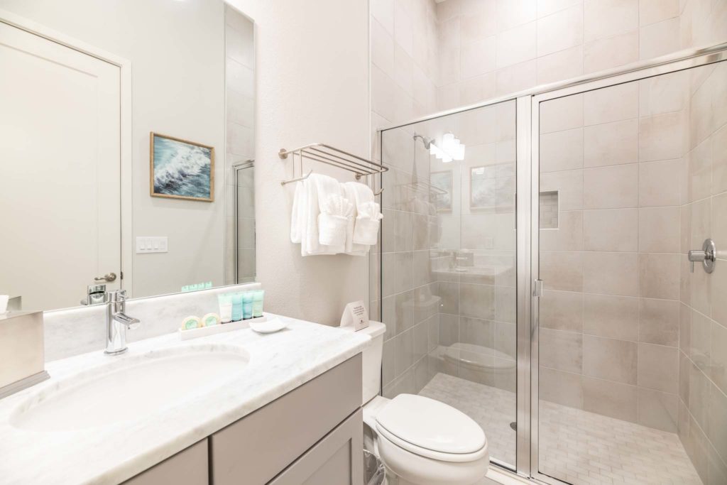 Furnished bathroom with toilet, sink, large mirror, and standing shower stall.
