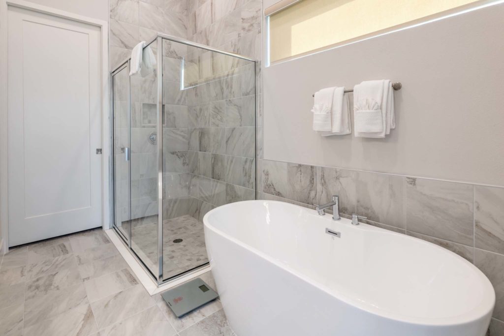 Modern freestanding bathtub and separate shower stall with glass doors.