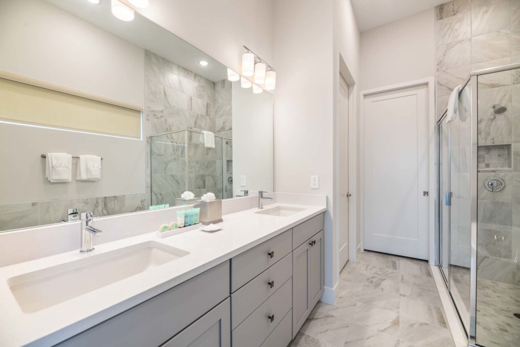 Double bathroom sink with large, wall-to-wall mirror next to a standing shower stall with glass doors.