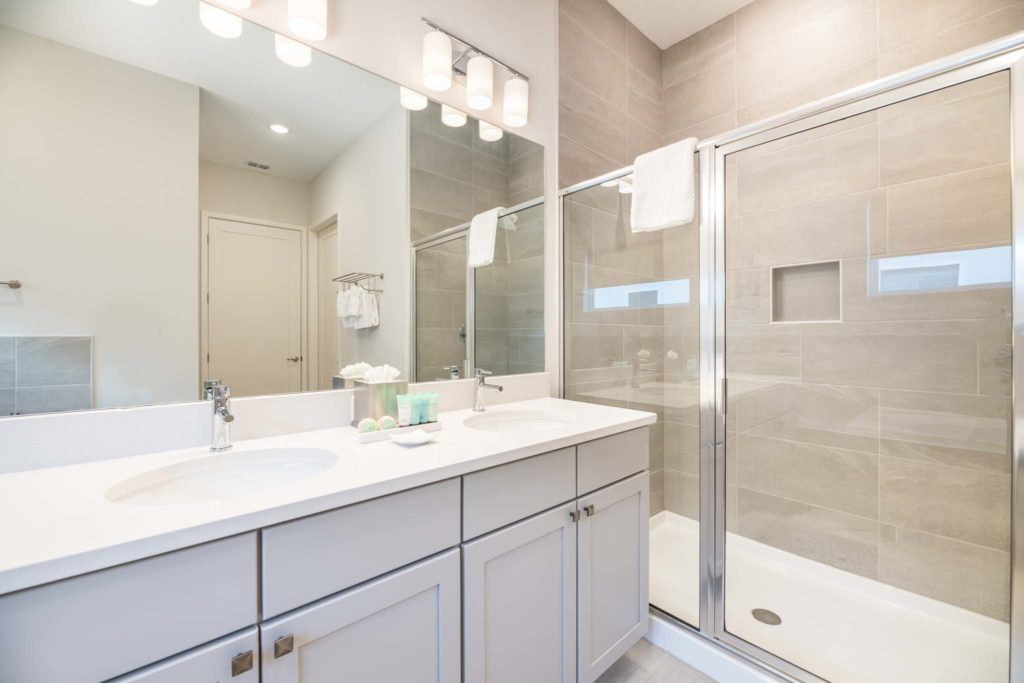 Bathroom with double sink, wall-to-wall mirror, and standing shower stall with glass doors.