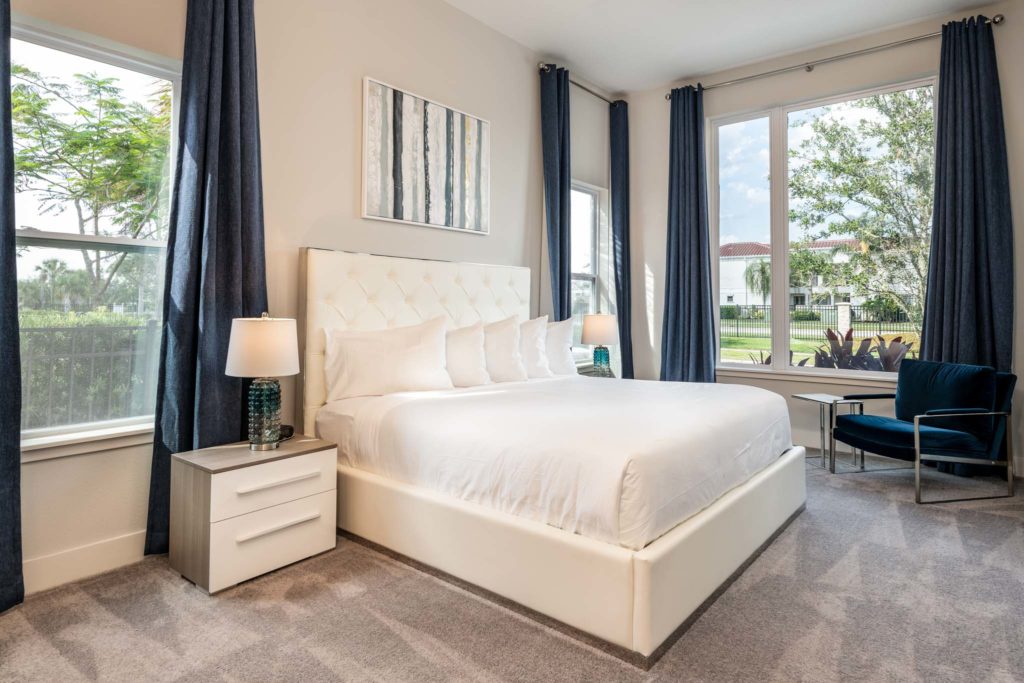 Bedroom with large king bed, plush headboard, armchair, and three large, open windows.
