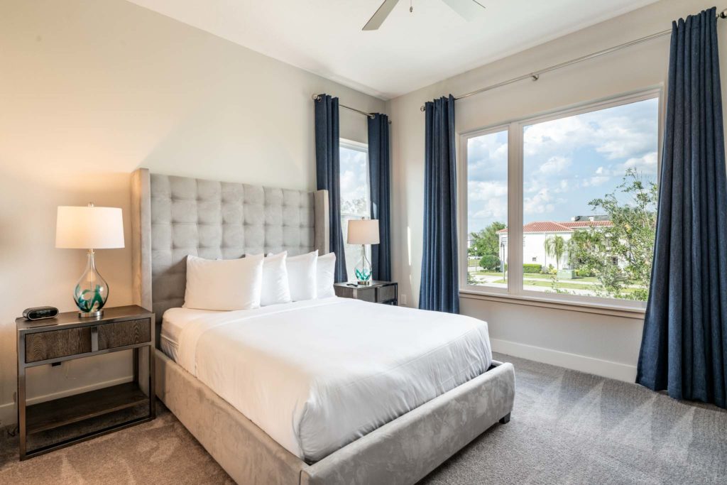 Bedroom with king bed, large plush headboard, and large open windows.