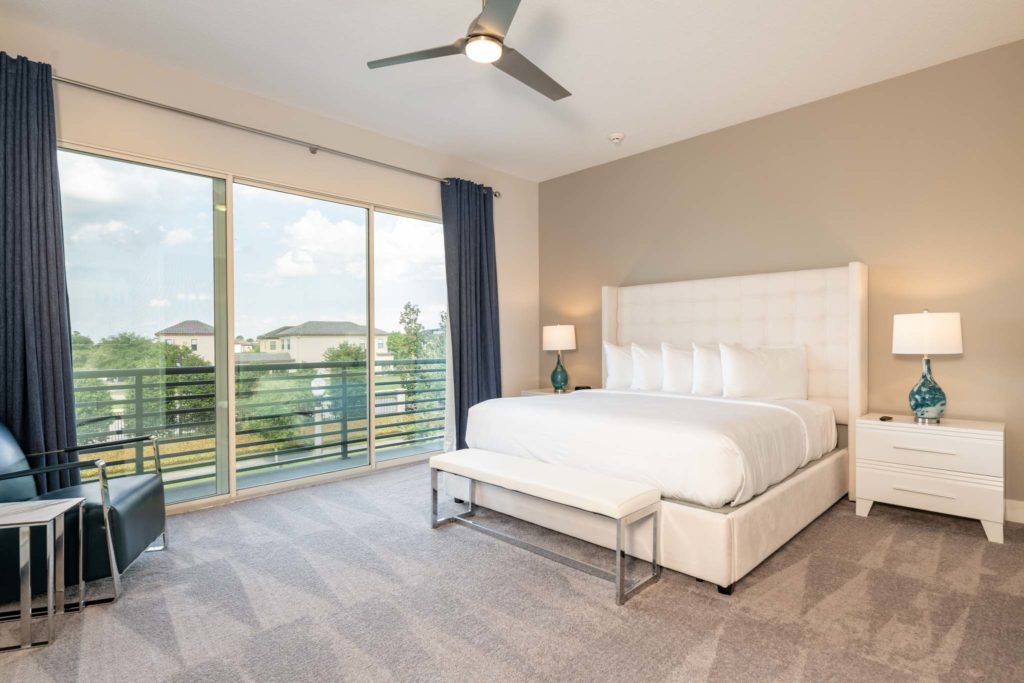 Spacious bedroom with large king bed, plush headboard, ceiling fan, and sliding door balcony access.