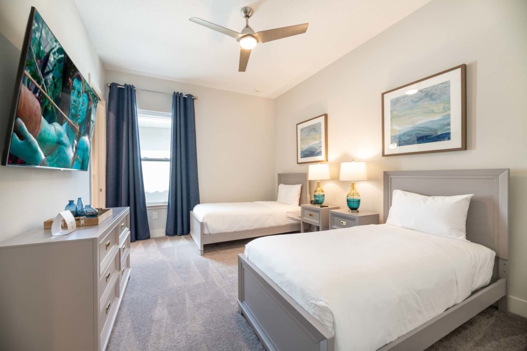Bedroom with twin beds, side tables, wall-mounted TV, long dresser, and window.