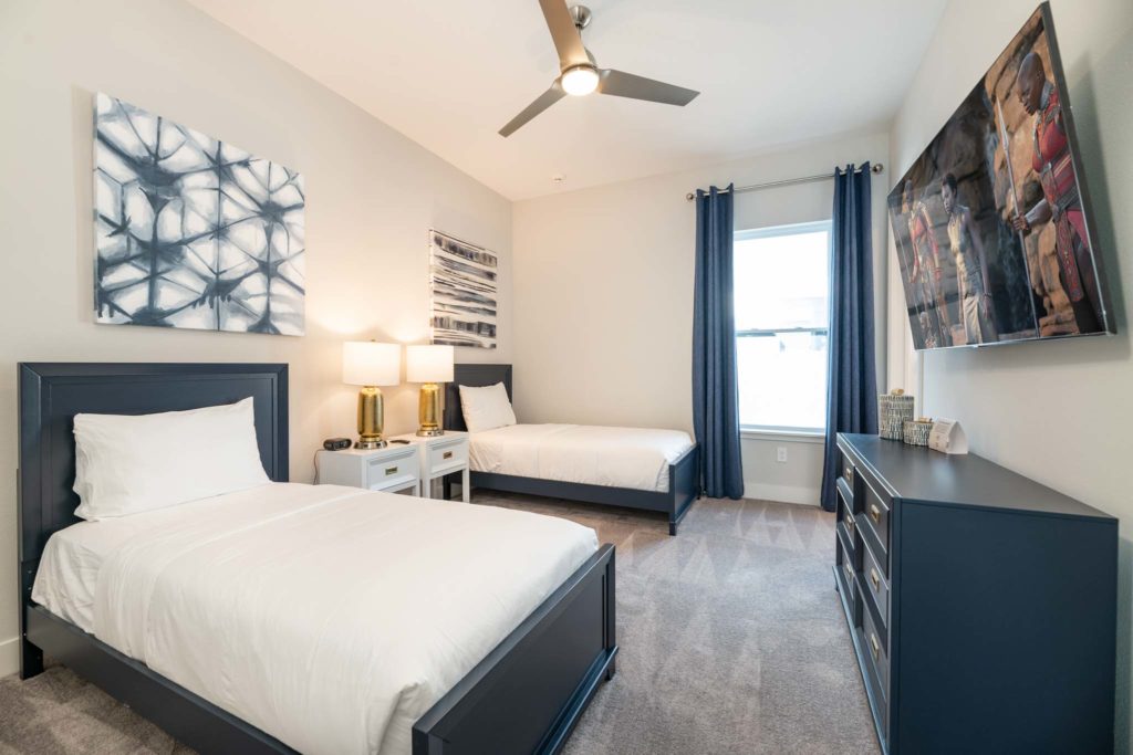 Bedroom with twin beds, wall-mounted TV, decorative wall art, long dresser, ceiling fan, and window.