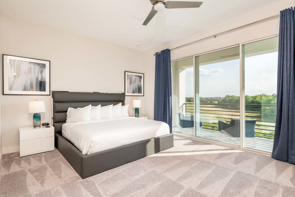 Spacious bedroom with large king bed, leather headboard, and sliding door balcony access.