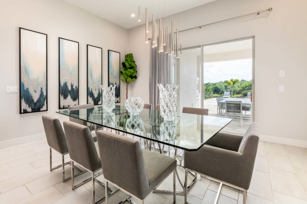 Modern dining room with decorative wall art and ceiling lights, with sliding door access to covered backyard lanai.
