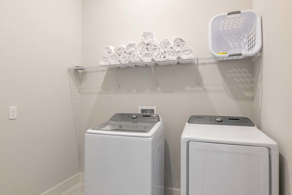 Laundry room with washer and dryer units, towels, and laundry basket.