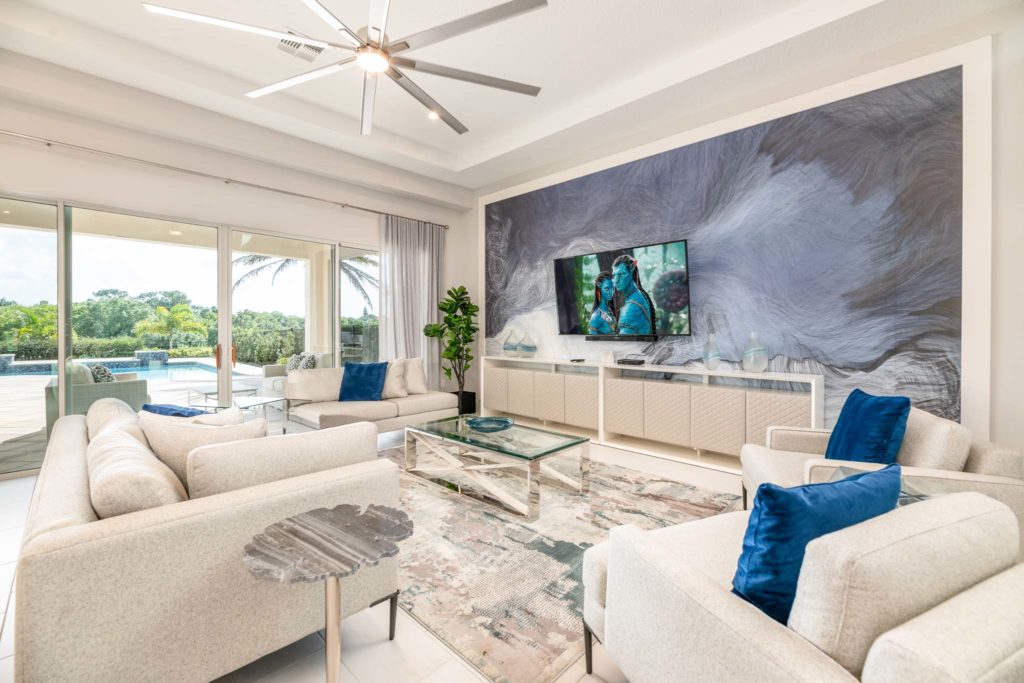Spacious living room with large, decorative wall art mural, large ceiling fan, and sliding door access to private pool.