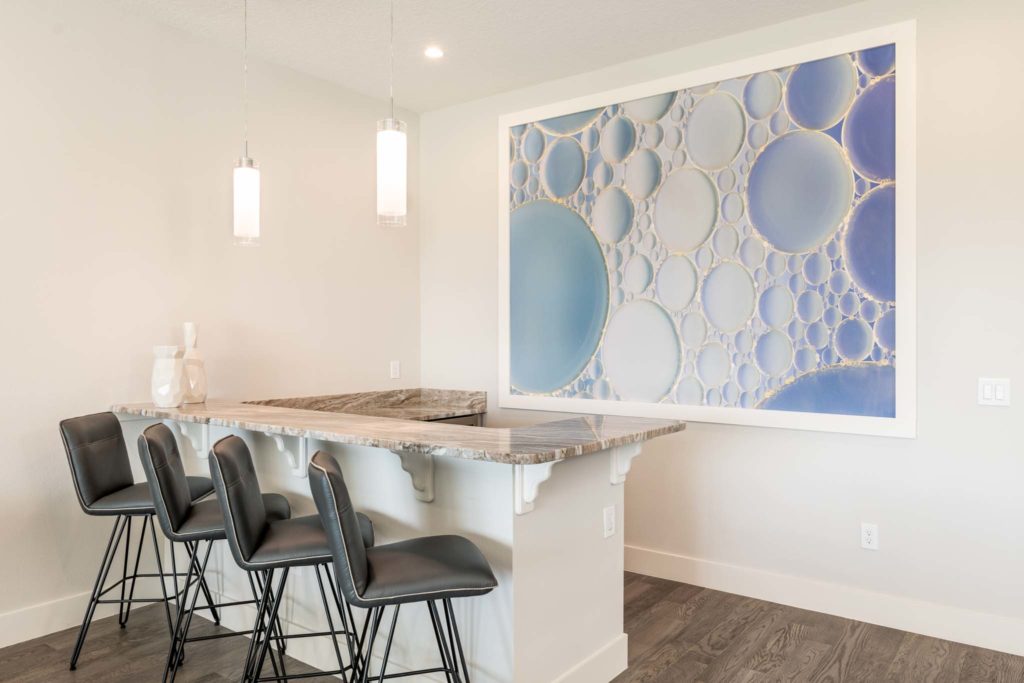 Upper loft dry bar with barstool seating in front of a large, decorative photo on the wall.