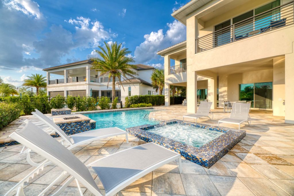 Private backyard of an 8-bedroom resort residence with pool, hot tub, lounge chairs, and covered summer kitchen.