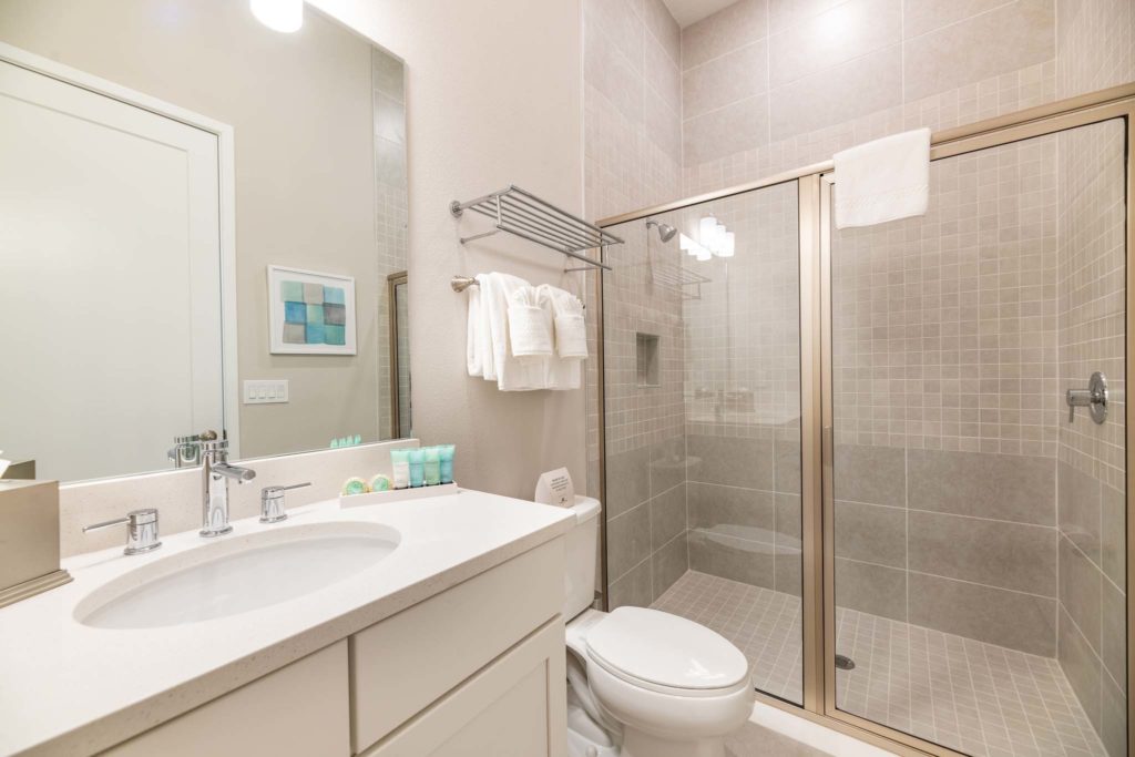 Bathroom with glass-door standing shower, toilet, sink, and mirror.