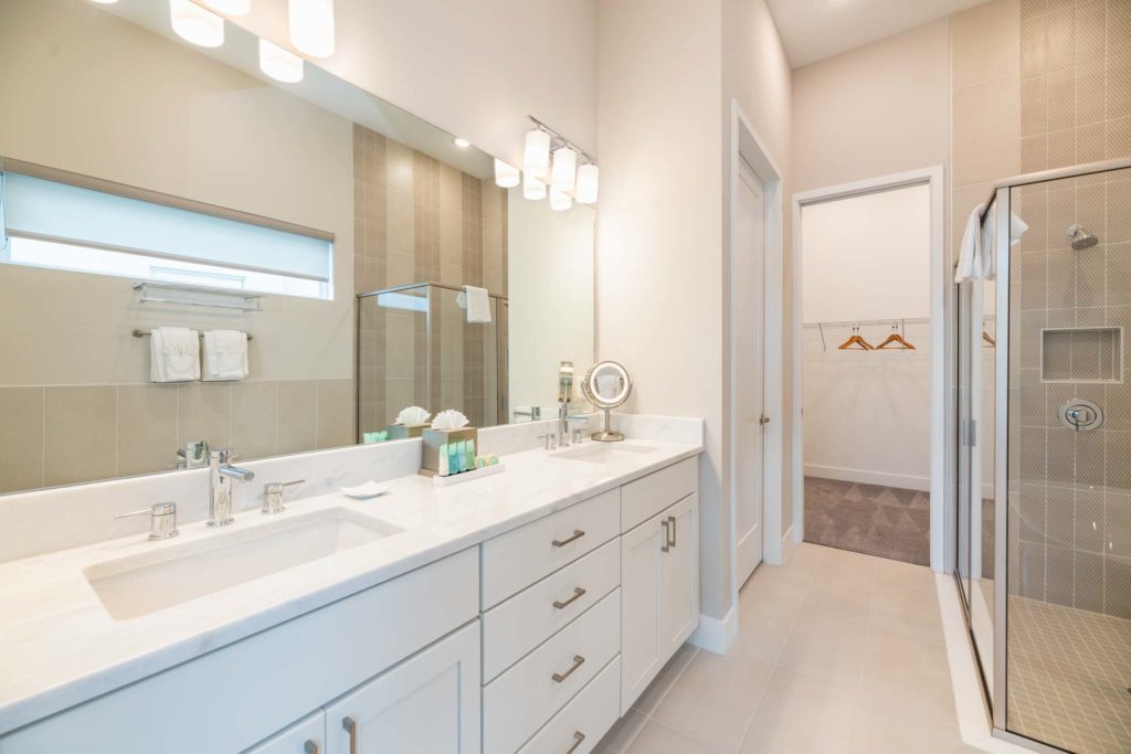 Large bathroom with double sink, wall-to-wall mirror, and glass-door standing shower.
