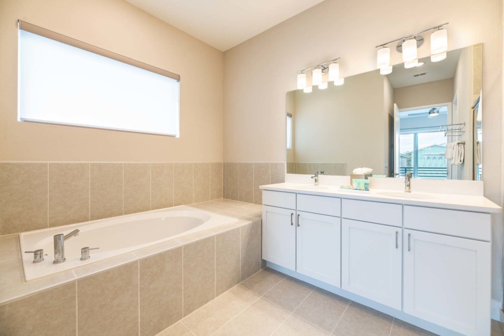 Bathroom with drop-in bathtub, double sink, and large mirror.