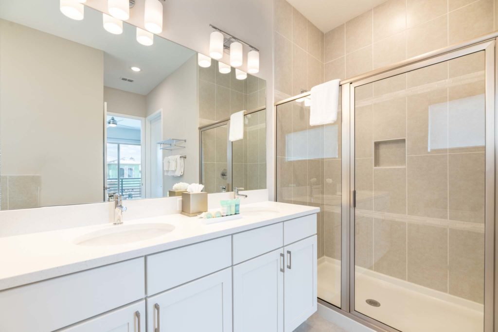 Bathroom with double sink, wall-to-wall mirror, and glass-door standing shower.