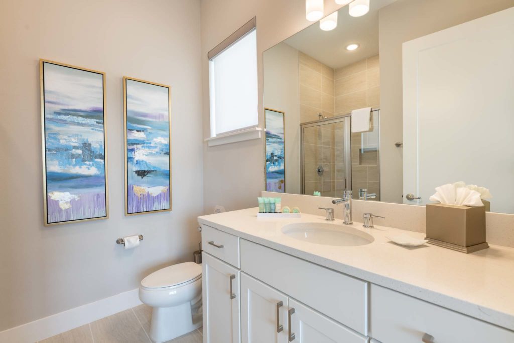 Bathroom with toilet, sink, wall-to-wall mirror, and glass door standing shower.