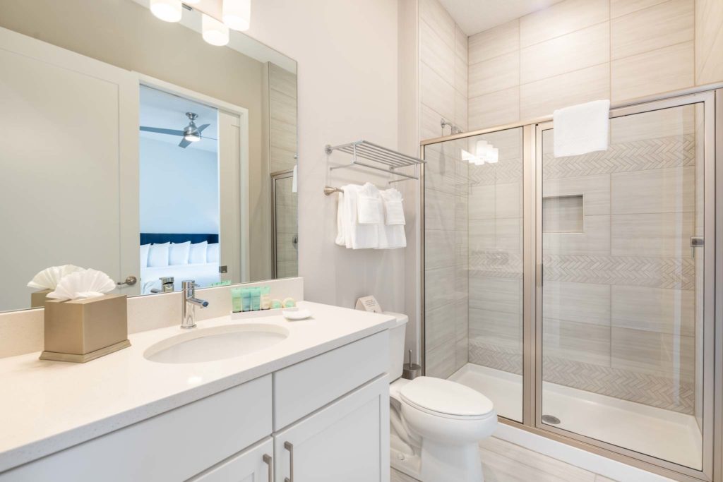 Bathroom with sink, mirror, toilet, and glass door standing shower.