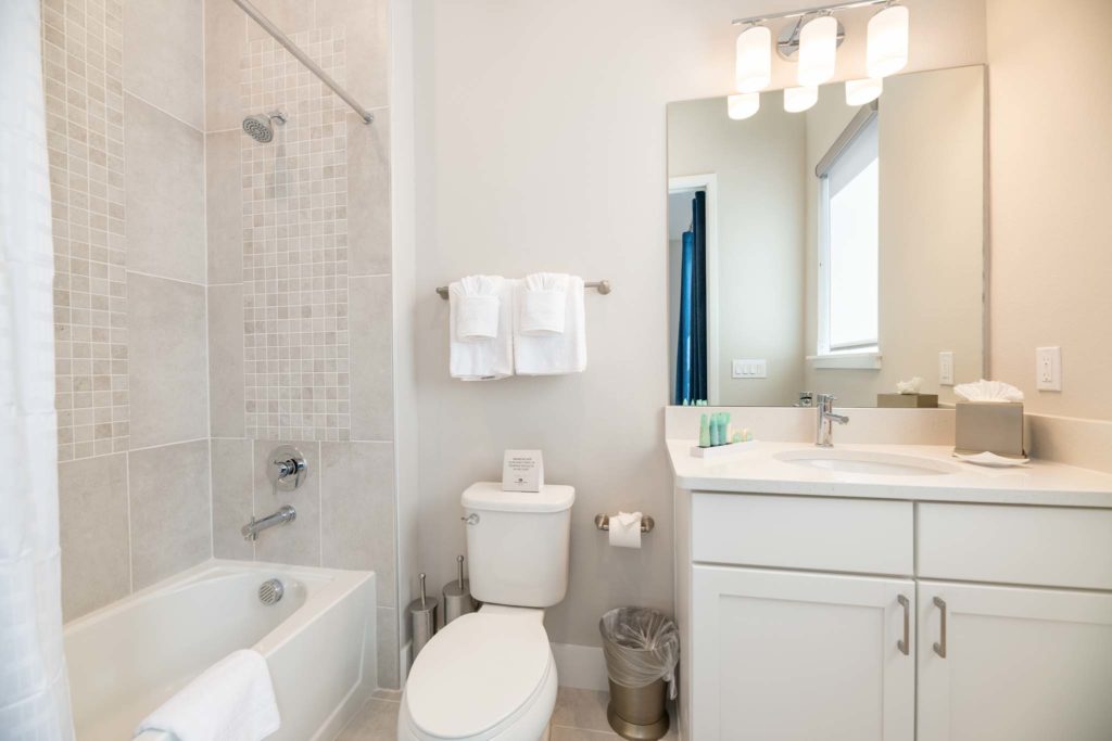 Bathroom with tiled alcove, bathtub, toilet, sink, and mirror.