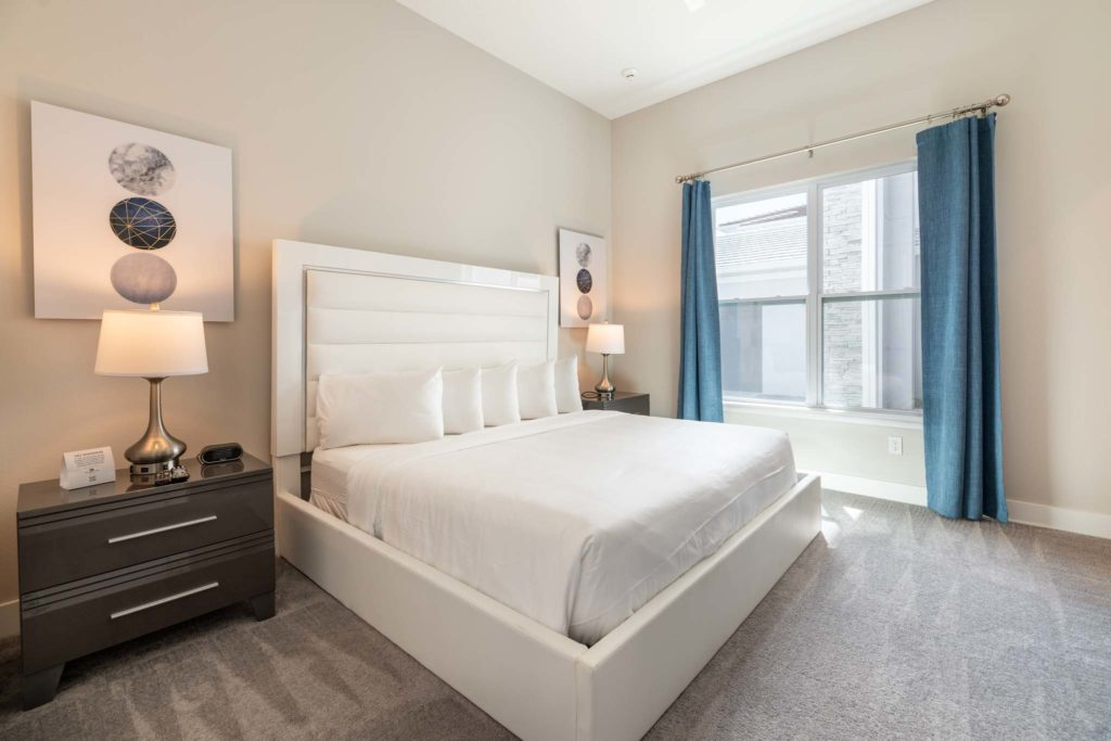 Bedroom with large king bed, plush headboard, side tables, decorative wall art, and large window.