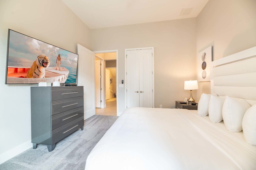 Large king bed with plush headboard facing a wall-mounted TV.