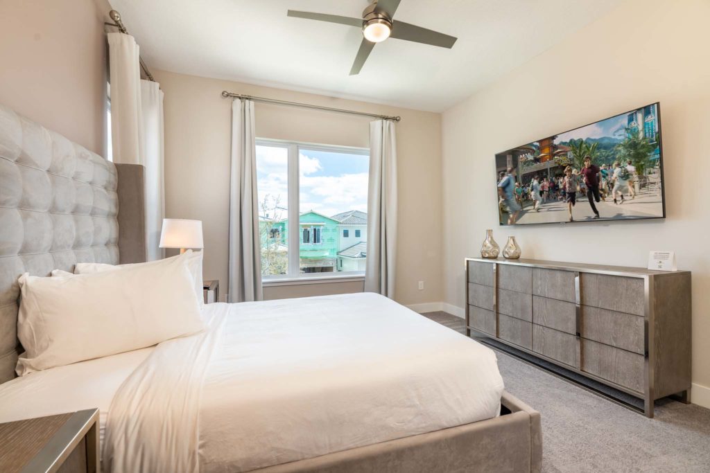 Large king bed with plush headboard facing a wall-mounted TV.