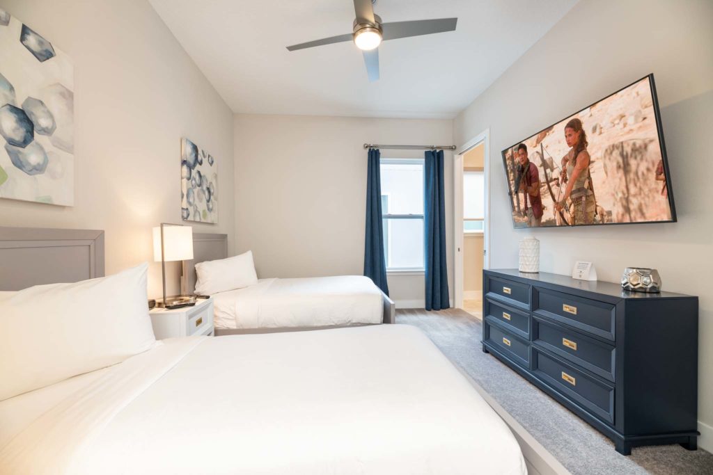 Twin beds facing a wall-mounted TV and long dresser.
