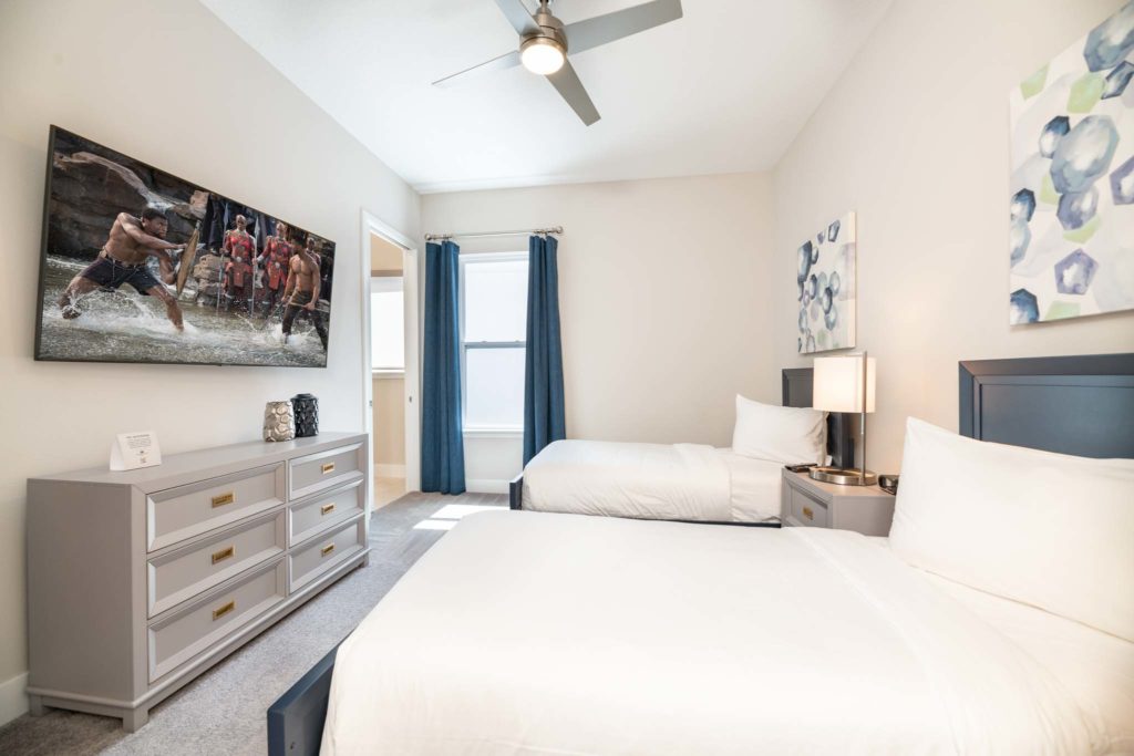 Twin beds facing a large, wall-mounted TV and long dresser.
