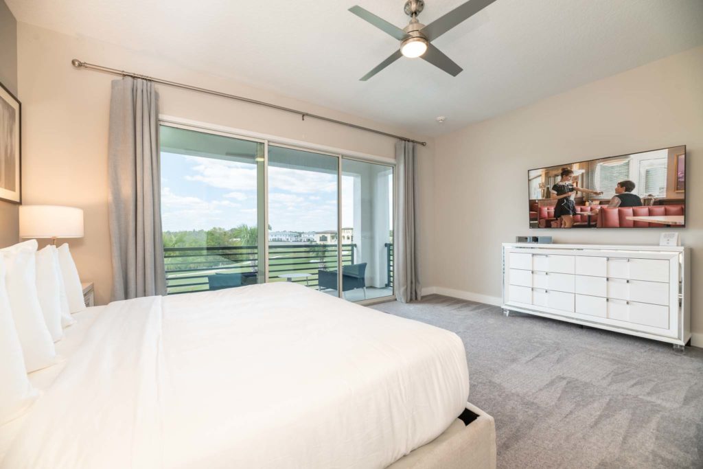 Spacious bedroom with large king bed, wall-mounted TV, and sliding door balcony access.