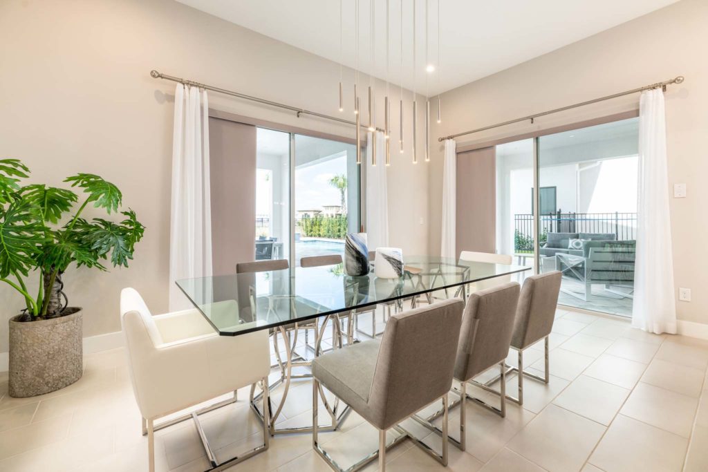 Glass dining room table with modern lighting and sliding glass door access to backyard private pool and covered lanai.