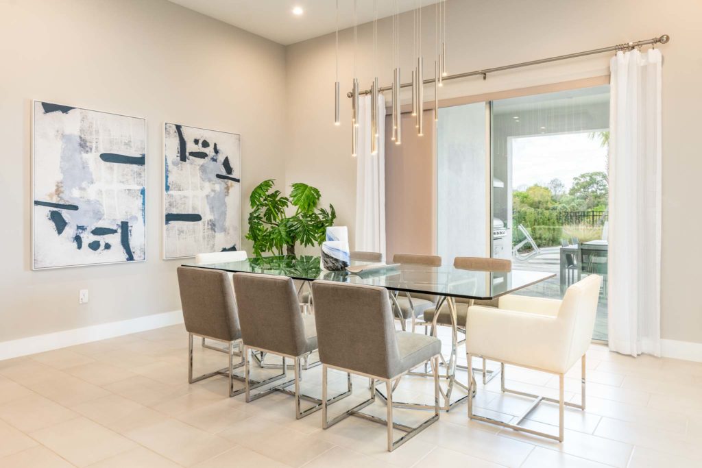 Spacious dining room with glass table, decorative wall art, and sliding glass door access to private pool and covered summer kitchen.