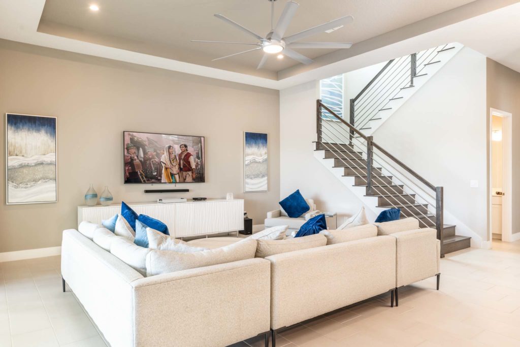 Living room with sectional sofa, wall-mounted TV, large ceiling fan, and stairs to the upper level.