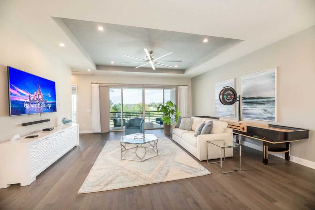 Spacious loft with sofa, shuffleboard table, electronic scoreboard, wall-mounted TV, and sliding door balcony access.