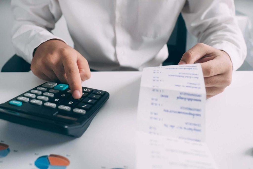 Person calculating a budget while using a calculator and looking at a receipt