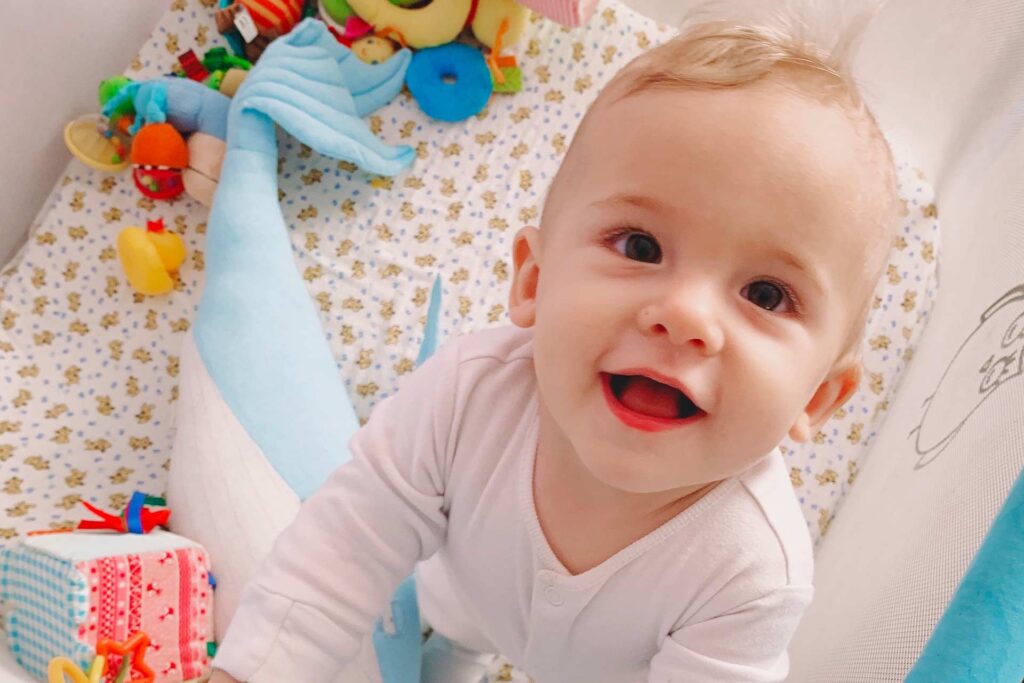Guest Equipment Rentals 2 Happy baby boy surrounded by toys in a pack 'n play crib