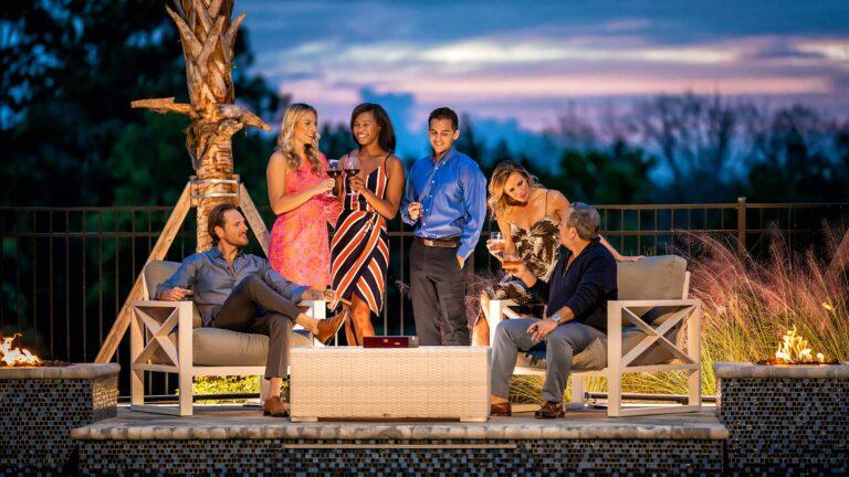 Group of adults enjoying cocktails by the outdoor fire pits of their resort residence at sunset.