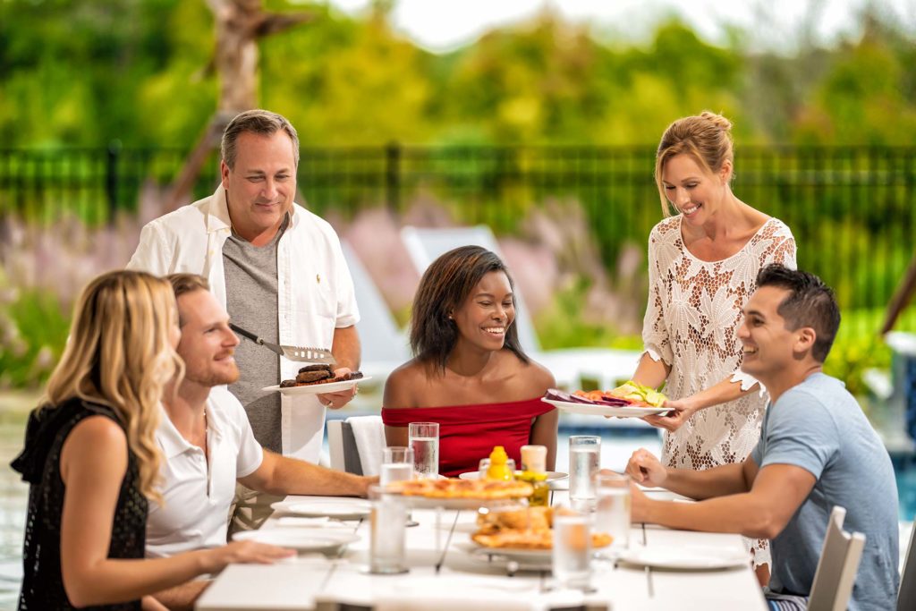 Groups 3 Group of adults gathered around a table of grilled food in the outdoor summer kitchen lanai of a Bear’s Den resort residence.