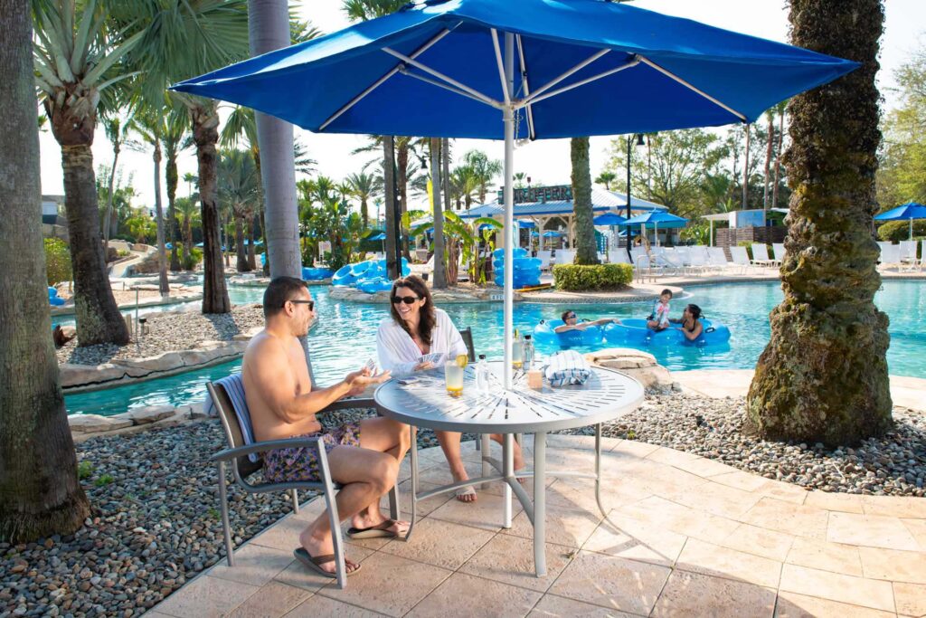 Couple playing a game of cards at a covered table next to the lazy river at the Reunion Resort Water Park