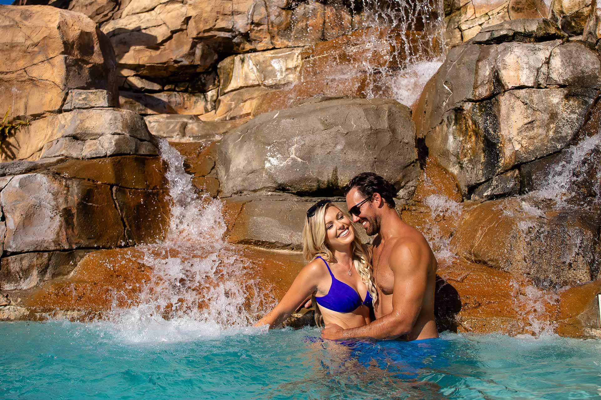 Happy couple standing in a pool by a waterfall at the water park | Bear's Den Resort Orlando