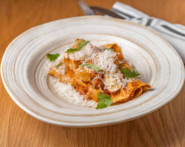 Plate of papardelle pasta with a red sauce topped with fresh basil and parmesan cheese