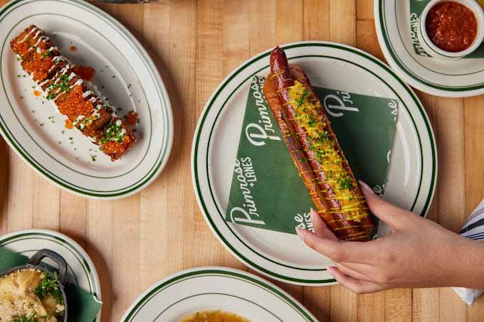 Various plates of elevated comfort foods including a hot dog