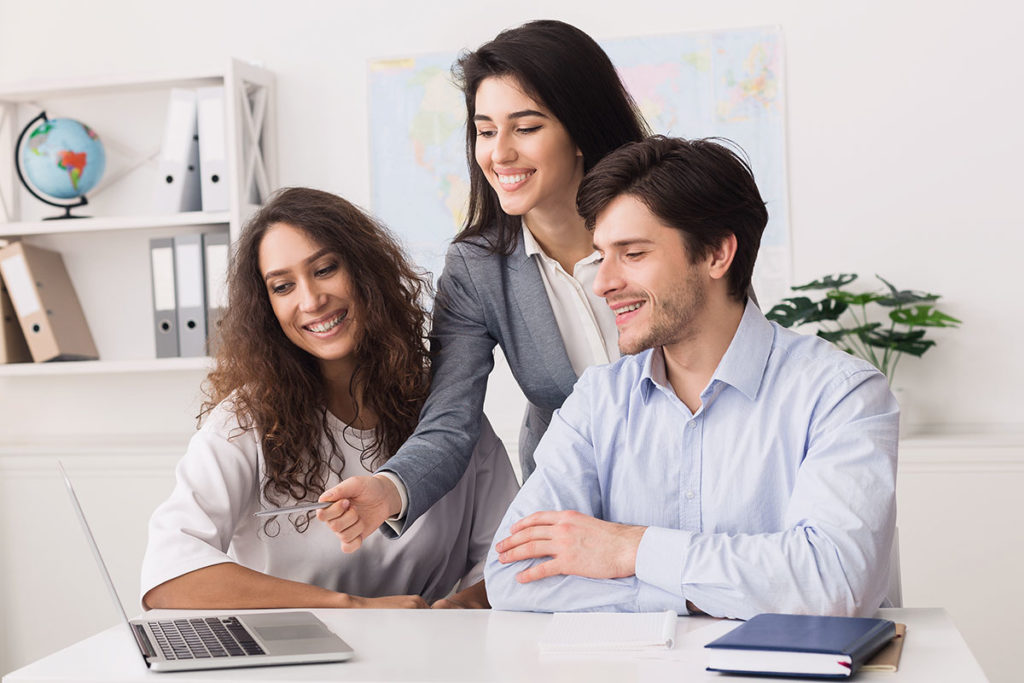 Travel agent points at laptop as she helps a couple plan a vacation getaway.