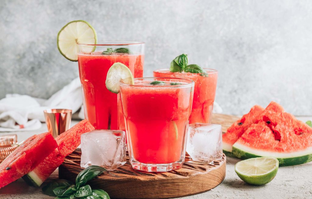 Watermelon lemonade with lime and fresh basil leaves on concrete background. Refreshing summer drink.