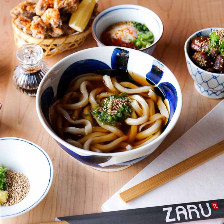 Bowl of udon noodles in a soup broth surrounded by various side dishes
